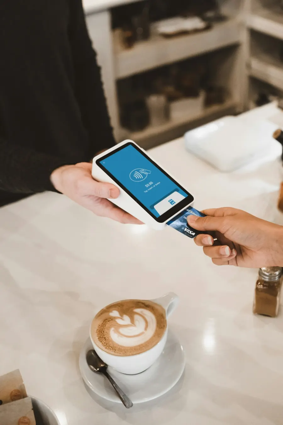 A customer pays by card at a café counter beside a latte