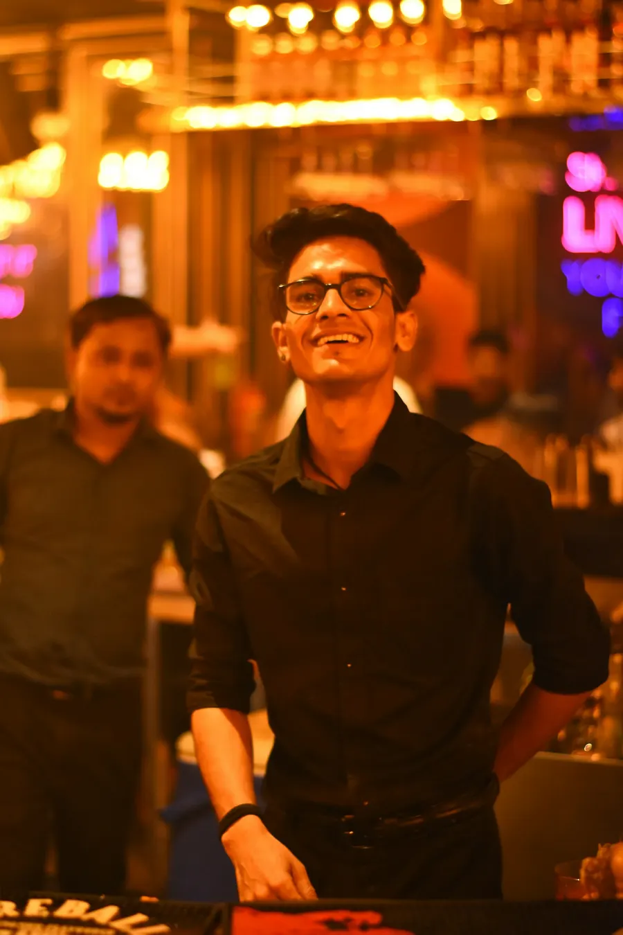 A smiling bartender behind a busy bar